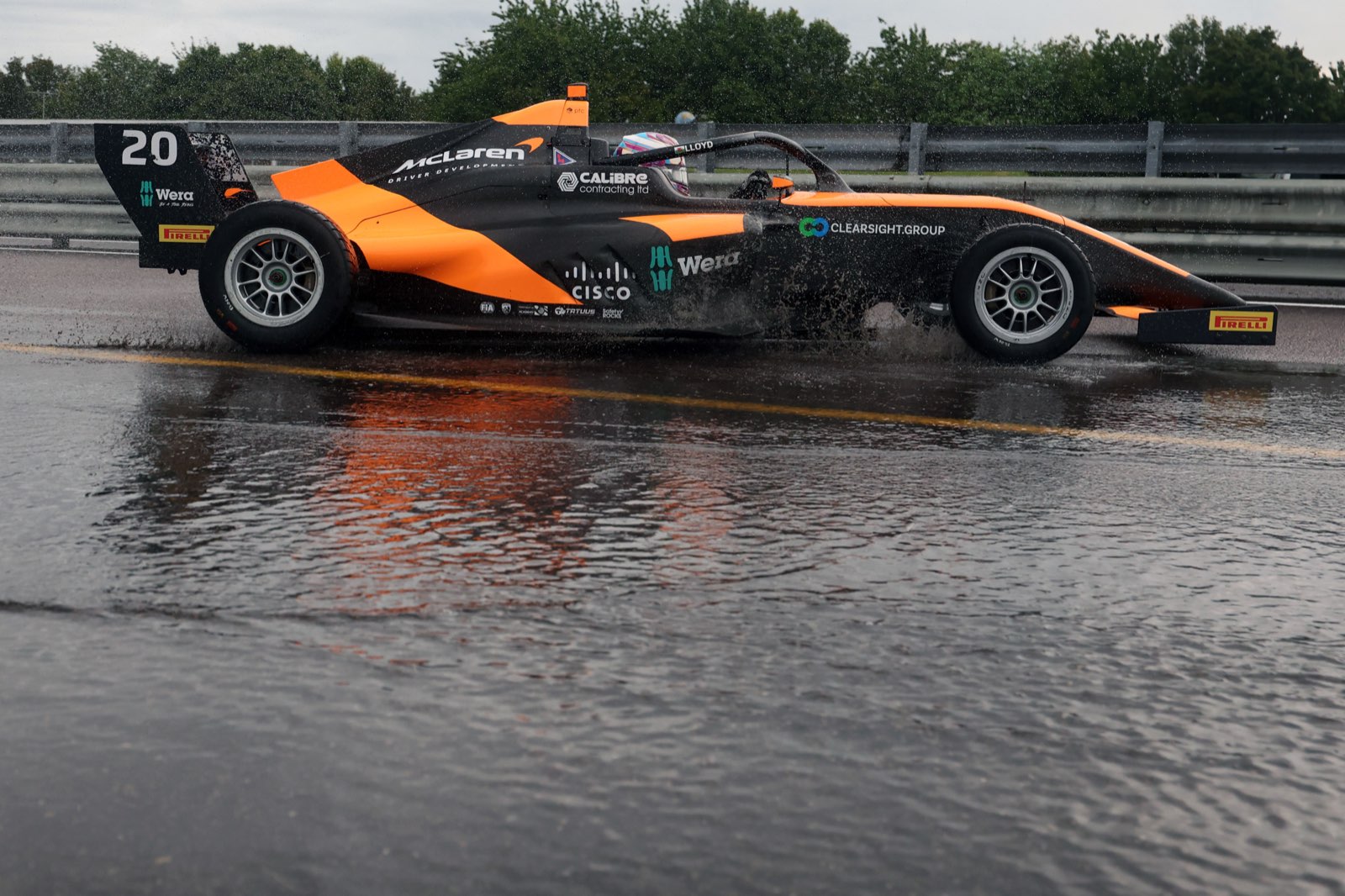 Side profile of Ella Lloyd's no. 20 McLaren F1 Academy car on a wet track, with Clearsight branding on the sidepod